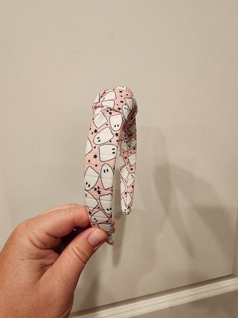 May include: A pink headband with a white ghost pattern. The headband is tied in a knot at the top.