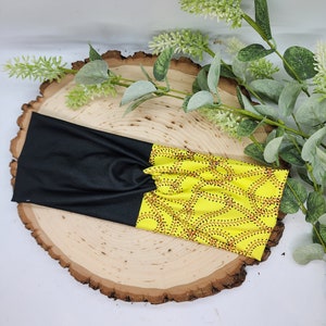 May include: A black and yellow headband with a pattern of red and black baseball stitches. The headband is on a wooden surface.
