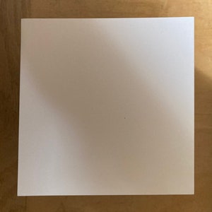 May include: A blank white sheet of paper on a wooden surface.