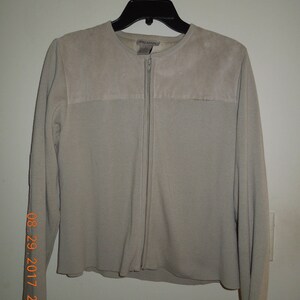 May include: A light beige zip-up sweater with a suede yoke. The sweater has long sleeves and a round neckline.