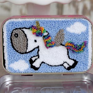 May include: Two small tin containers with pink lids, each containing a hand-stitched felt unicorn with a rainbow mane and tail. The containers are labeled "Altoids".