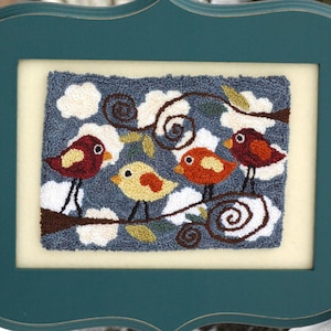 May include: A framed needlepoint artwork featuring three birds perched on a branch with white clouds and swirling vines in the background. The birds are red, yellow, and orange.