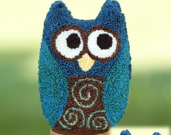 May include: A blue and green owl with brown swirls, made with yarn and displayed on a wooden stand. A smaller owl with the same design is shown to the right.