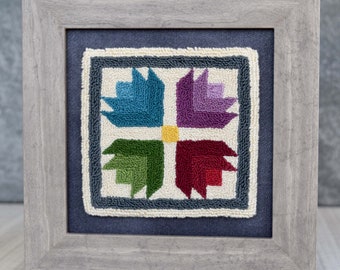 May include: A framed needlepoint design featuring a colorful geometric pattern with four sections of blue, purple, green, and red. The design is set against a white background and framed in a gray wood frame.