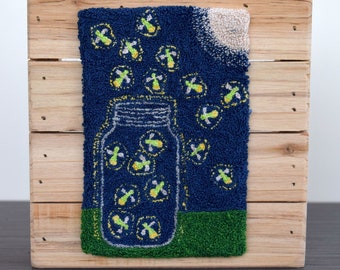 May include: A blue and green needlepoint design of a glass jar filled with glowing fireflies against a dark blue background with a white moon.