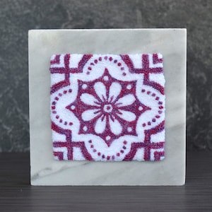 May include: A white square tile with a pink and white floral design. The tile is framed by a white border and is set against a gray background.