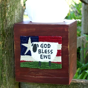 May include: A red wooden tissue box holder with a white sheep and an American flag design. The design says "God Bless Ewe".