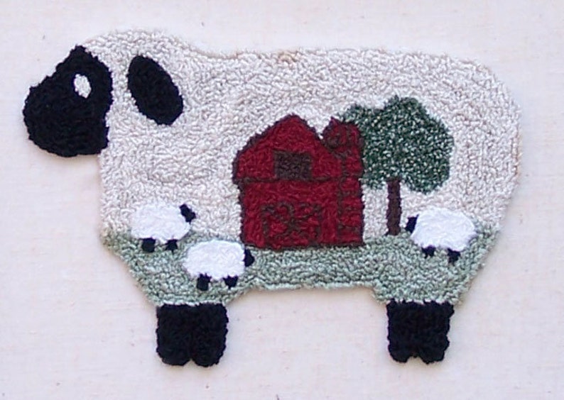 May include: A white sheep rug with black legs and a black face. The sheep is standing in a field with a red barn, a green tree, and three smaller white sheep.