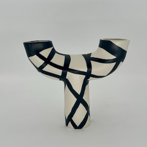 May include: A cream-colored ceramic vase with a unique Y-shape design. The vase features black geometric patterns and accents. The top and the base of the vase are black. The vase is a decorative item.