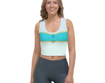 May include: A white crop top with a blue and gold design. The design features a blue gem in the center of a gold band.