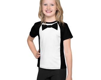 May include: A black and white t-shirt with a tuxedo design. The shirt has a white front with a black bow tie and black sleeves.
