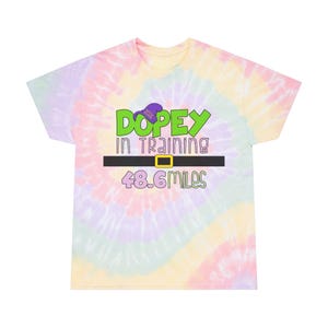 May include: A tie-dye t-shirt with a colorful swirl pattern. The shirt features a green cartoon image of Dopey from Disney's Snow White and the Seven Dwarfs wearing a purple hat. The text "Dopey in Training 48.6 miles" is printed on the shirt.