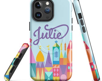 Puede incluir: Una funda de teléfono azul claro con el nombre "Julie" en escritura morada. La funda presenta un diseño de castillo colorido con varias formas y colores. El lateral de la funda tiene un patrón geométrico colorido.