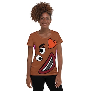 Puede incluir: Una camiseta marrón con una cara de dibujos animados impresa en la parte delantera. La cara tiene una boca roja grande, dos ojos negros, una nariz rosa y una oreja naranja.