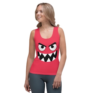 May include: A red tank top with a black and white cartoon monster face graphic. The monster has large eyes, a wide grin, and sharp teeth.