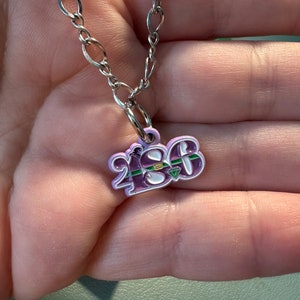 May include: A silver chain necklace with a purple pendant featuring the number "2186" with green accents and a diamond.