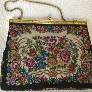 May include: A vintage floral tapestry evening bag with a gold chain strap and a gold clasp. The bag features a floral design with pink, red, blue, and green flowers on a cream background.