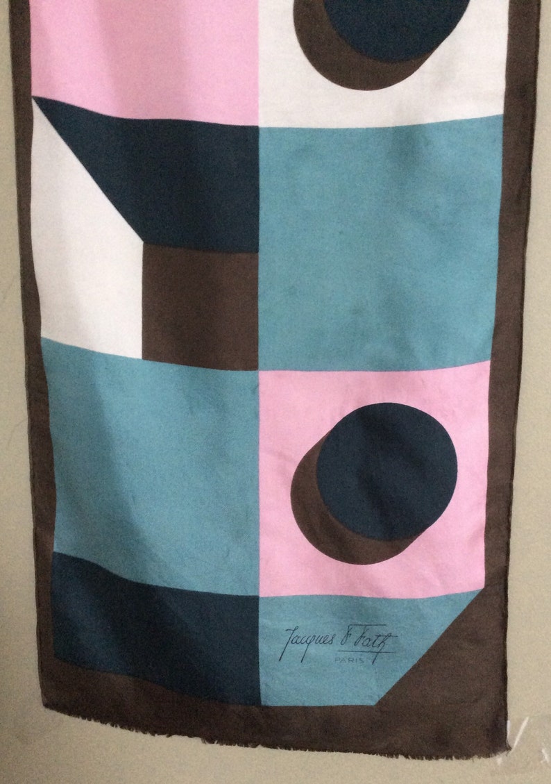 May include: A vintage scarf with a geometric design in pink, teal, white, and brown. The scarf features a repeating pattern of squares, circles, and triangles. The Jacques Fath Paris signature is visible.