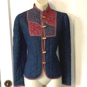 May include: A quilted denim jacket with a red and blue patchwork design on the front. The jacket has a mandarin collar and wooden button closures.