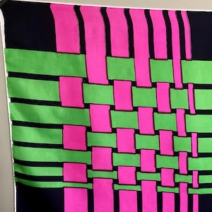 May include: A colorful textile with a woven pattern. The design features a grid of bright pink and green rectangles, set against a black background. The edges are finished with a white border.