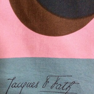 May include: A pink, teal, and brown patterned scarf. The design features large, overlapping circles in brown and teal against a pink background. The words "Jacques & Fath PARIS" are printed in black.