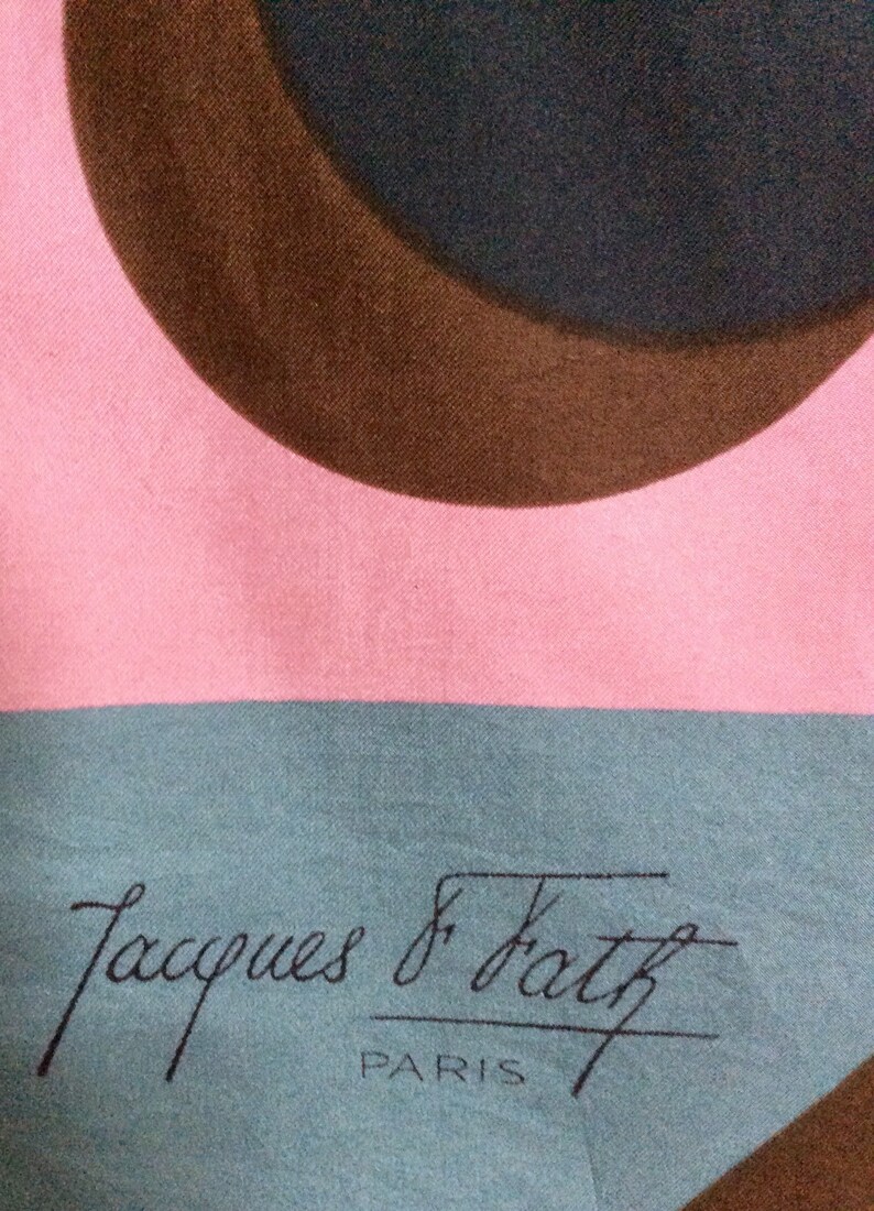 May include: A pink, teal, and brown patterned scarf. The design features large, overlapping circles in brown and teal against a pink background. The words "Jacques & Fath PARIS" are printed in black.