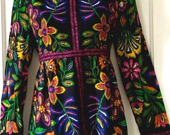 May include: A long-sleeved black dress featuring a vibrant, multi-colored floral pattern in shades of yellow, orange, pink, green, and blue. The garment includes a high collar with ruffled trim, a fitted waistline, and matching decorative piping.