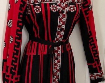 May include: A vintage long-sleeve dress in red and black, featuring a geometric and floral pattern. The dress has a collared neckline, button-down front, and a black belt. The dress is displayed on a mannequin.