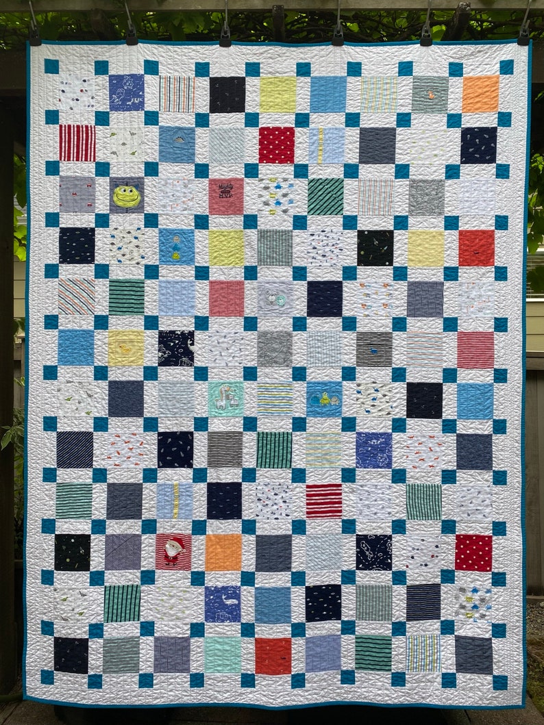 May include: A patchwork quilt featuring a grid of multi-colored fabric squares in various patterns, including stripes, polka dots, and cartoon graphics. The squares are separated by a teal blue lattice border and finished with a matching teal blue edge.