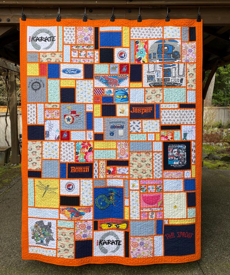May include: A rectangular memory quilt featuring a vibrant orange border and a patchwork design of various fabric squares. The quilt includes printed graphics such as the word Karate, a Ford logo, R2-D2, the name Jasper, and Barack Obama.