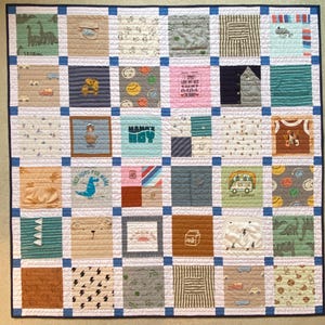 May include: A square patchwork quilt constructed from various fabric squares featuring diverse patterns, colors, and graphics including dinosaurs, vehicles, and text like "I ONLY LOVE MY BED AND MY MAMA I'M SORRY" and "MAMA'S BOY", separated by blue sashing.