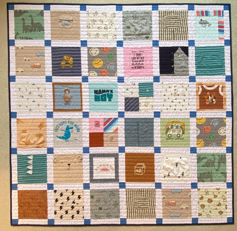 May include: A square patchwork quilt constructed from various fabric squares featuring diverse patterns, colors, and graphics including dinosaurs, vehicles, and text like "I ONLY LOVE MY BED AND MY MAMA I'M SORRY" and "MAMA'S BOY", separated by blue sashing.