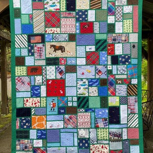 May include: A patchwork quilt featuring a green border and numerous rectangular fabric blocks in various patterns, including plaid, stripes, stars, and animal prints. Several blocks display embroidered motifs like a horse, a knight, and the letters JR.
