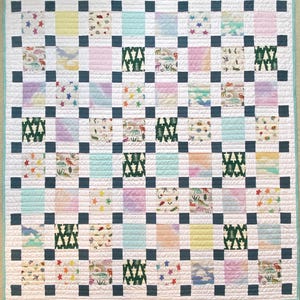 May include: A square patchwork quilt featuring a grid of alternating patterned and solid-colored fabric squares. The design includes dark blue sashing, white borders, and a light teal edge binding. Patterns include pine trees, stars, and dinosaurs.