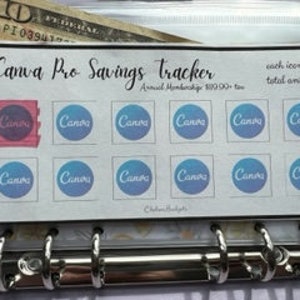 May include: A savings tracker with the text "Canva Pro Savings tracker" and the words "each icon $11 total amt: $130". The tracker has 12 blue circle icons and one pink square icon. A ten-dollar bill is visible behind the tracker.