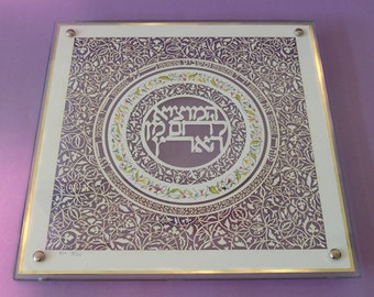 May include: A framed piece of art with a circular design featuring Hebrew text and intricate floral patterns in shades of purple, white, and gold.