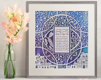 Könnte beinhalten: Ein gerahmtes Papier-Schnittkunstwerk mit einem blauen und violetten Aquarellhintergrund. Die Kunst zeigt einen hebräischen Segen für ein Zuhause, umgeben von filigranen weißen Papierschnitten von Blumen, Ranken und einer Stadtlandschaft. Der Text lautet: "Möge dieses Haus ein Ort des Glücks und der Gesundheit sein, ein Ort der Zufriedenheit, der Großzügigkeit und der Hoffnung, ein Zuhause der Kreativität und der Freundlichkeit. Mögen diejenigen, die es besuchen und hier leben, nur Segen und Frieden erfahren."
