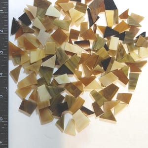 May include: A collection of irregularly shaped glass mosaic tiles in shades of brown, tan, and cream. A ruler is placed along the left side, with measurements in inches. The tiles are scattered on a white surface. The text "debscolorfulcorner" is in the bottom right corner.