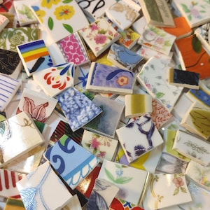 May include: A collection of colorful, broken ceramic tiles with various floral, geometric, and abstract patterns. The tiles are in shades of blue, white, yellow, orange, and pink. Some tiles have visible text. The image is from debscolorfulcorner.