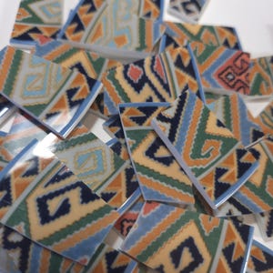 May include: A collection of rectangular ceramic mosaic tiles featuring a repeating geometric pattern in shades of orange, green, light blue, and dark navy blue. The tiles have a smooth, glossy finish and are scattered across a white surface.