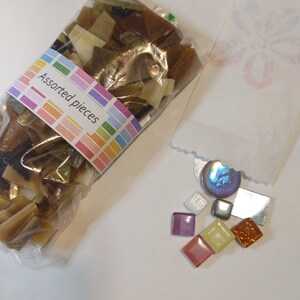 May include: A clear plastic bag filled with assorted brown and tan mosaic pieces, next to a small bag with colorful square tiles. The label on the bag reads "Assorted pieces" in a rainbow-colored font.