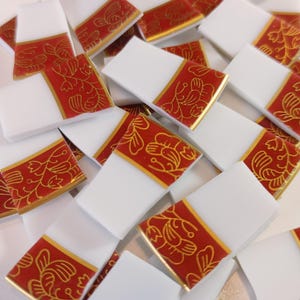 May include: A collection of white rectangular tiles with a red and gold floral design. The tiles are scattered, showcasing the decorative pattern. The design features a red band with gold floral motifs.