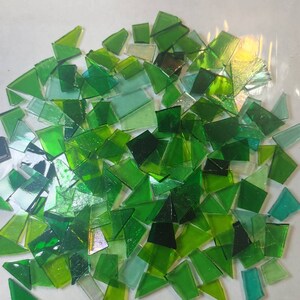 Puede incluir: Un conjunto de teselas de mosaico de vidrio verde de formas irregulares. Los tonos de verde var&iacute;an de claro a oscuro, algunas piezas son transl&uacute;cidas. Se ve una regla negra con marcas blancas.