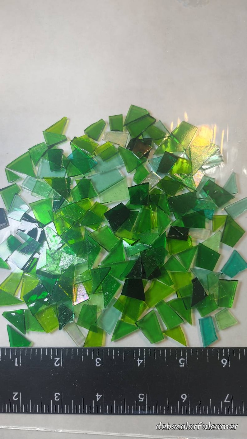 Puede incluir: Un conjunto de teselas de mosaico de vidrio verde de formas irregulares. Los tonos de verde var&iacute;an de claro a oscuro, algunas piezas son transl&uacute;cidas. Se ve una regla negra con marcas blancas.