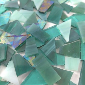 May include: A collection of irregularly shaped, teal and turquoise glass mosaic tiles. The tiles vary in size and shape, with some appearing translucent and others opaque. The image is well-lit, showcasing the different shades of green and blue.