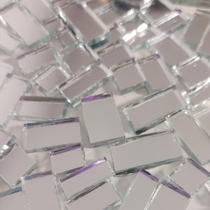 May include: A collection of small, rectangular, mirrored glass tiles. The tiles are silver with a reflective surface and a hint of purple along the edges. The text "Debscolorfulcorner" is visible in the bottom right corner.