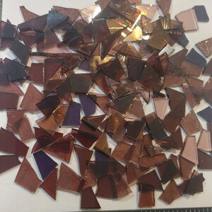 Puede incluir: Un conjunto de piezas de vidrio de colores de forma irregular, en tonos marrones, morados y dorados. Los fragmentos de vidrio est&aacute;n dispersos sobre una superficie blanca, con una regla negra para la escala. Piezas para arte de mosaico.