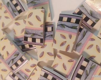 May include: A collection of decorative ceramic tiles with a repeating pattern. The tiles feature a cream-colored background with purple leaf shapes, and sections with black and white checkered patterns, and lavender and pink stripes.