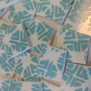 May include: A collection of white ceramic tiles with a teal blue geometric pattern. The tiles are square and have a glossy finish.