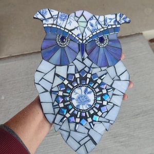 May include: A blue and white mosaic owl with a floral design. The owl's eyes are made of blue and white glass tiles.